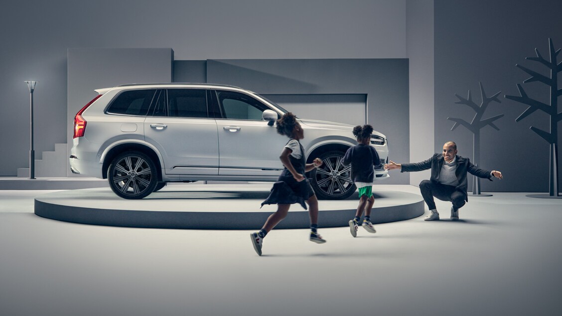 Kids running towards their dad in front of a Volvo